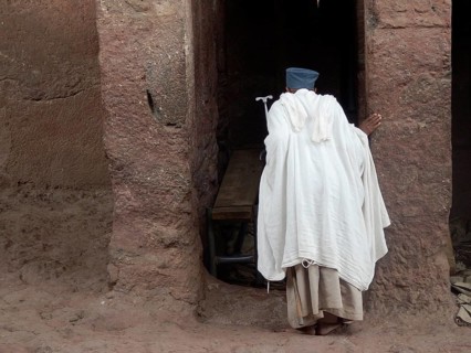 A man in traditional clothing stands at the entrance of an old stone structure, UNESCO World