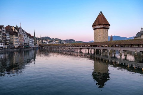 Historic wooden bridge and water tower in Lucerne at dusk with calming reflection in the water and