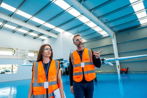 Experienced aviation engineers. Wearing safety vests and glasses. Discussing aircraft details while