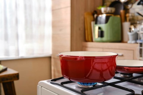 A red cast iron pot with enamelled coating on a gas stove in a kitchen. The kitchen has a blend of