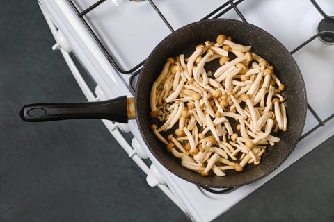 Cooking mushrooms in pan on stovetop in kitchen during daylight hours