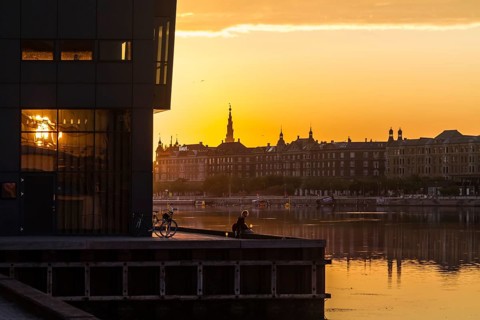 Silhouetten einer städtischen Skyline bei Sonnenuntergang mit ruhigem Wasser im Vordergrund,