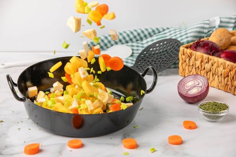 Fresh soup vegetables fall into a cooking pot next to ingredients and kitchen utensils