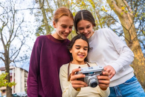 Three smiling sisters or friends discovering the functions of an old camera while enjoying a lovely