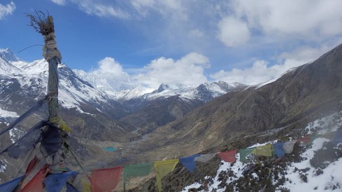 Wide mountain landscape with colorful prayer flags and snow-capped peaks under blue sky, trekking