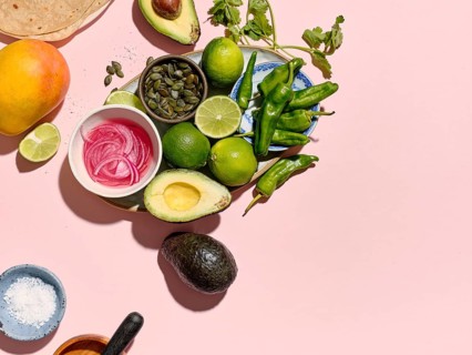 Top view of a vibrant taco preparation scene on a pink background. Ingredients like avocados,