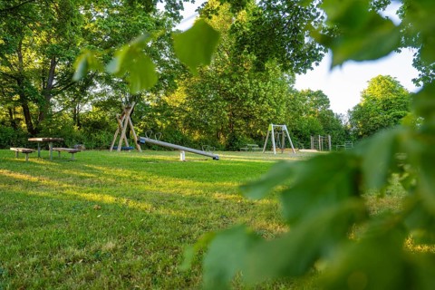 A playground with a seesaw on a green field surrounded by thick trees, Gechingen playgrounds, Calw