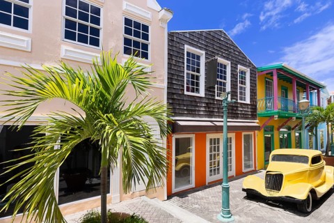 A yellow vintage car parked on a vibrant colonial street with colorful buildings, a palm tree and a