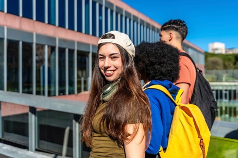 Young diverse students walking on a sunny university campus, carrying backpacks and smiling