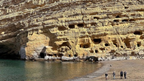 Rock formation with caves on the edge of a beach, small group of people on the shore, Matala,