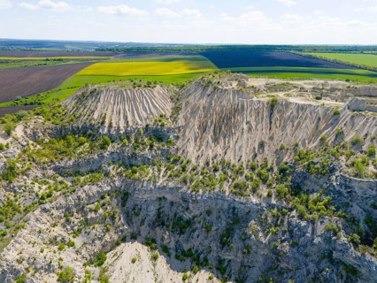 Dramatic rock formation with erosion-shaped cliffs surrounded by green fields under clear sky,