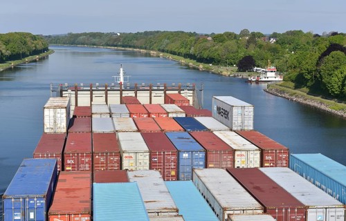 Giant container ship transports containers on river, green landscape, blue sky, container ship