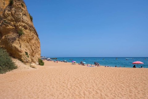 Quiet sandy beach with few people and umbrellas, rocks in the background, Albufeira, Faro, Portugal