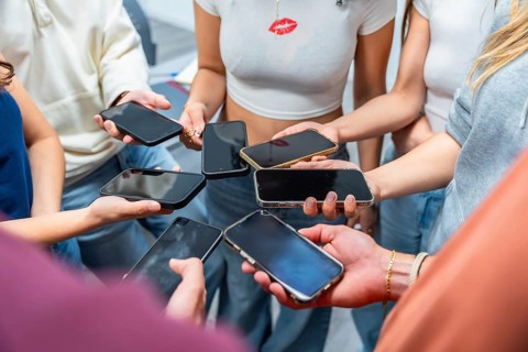 Teenagers are holding many mobile phones, forming a circle with their hands and connecting through
