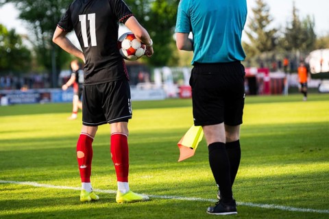 Soccer player waiting near the touchline with a ball beside the referee during a football match in