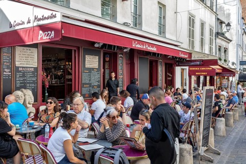 People enjoying drinks in a busy café with a red awning, Paris
