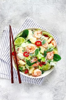 Thai salad with shrimp and rice noodles, pineapple slices, coriander and mint leaves, on a white