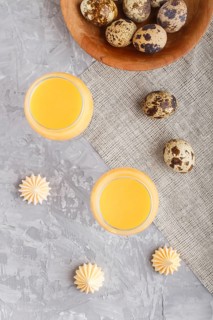 Sweet egg liqueur in glass with quail eggs and meringues on a gray concrete background. Top view,