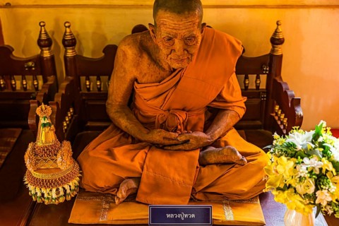 Wax figure of a seated Buddhist monk in orange robe, Wat Phra Singh Buddhist temple complex, Chiang