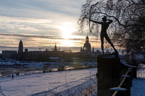 Bronze figure The archer in the snow, in the background the Elbe with drift ice and the old town
