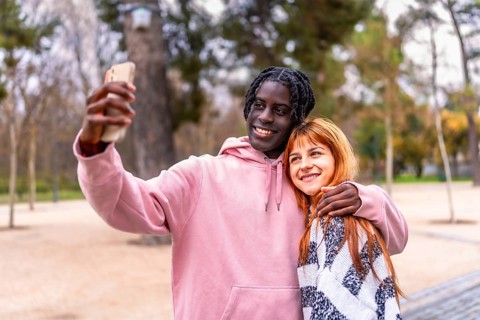 Young multiracial couple smiling and capturing a joyful selfie with a smartphone while enjoying a