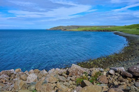 Rocky coast with sweeping views over the blue sea and green fields under a cloudy sky, Isle of