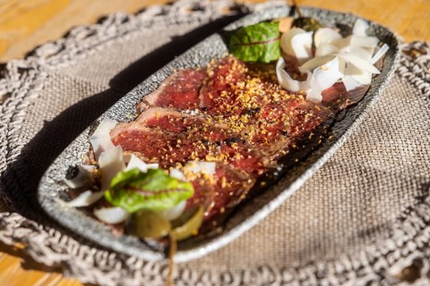 Freshly prepared venison carpaccio adorned with grated parmesan, spices, and a touch of fresh