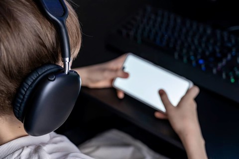 A teenager wearing headphones is deeply engaged in gaming on a smartphone. The image captures the