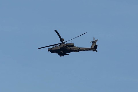 Apache AH-64E military helicopter aircraft of the Royal Army air corp flying in a blue sky,