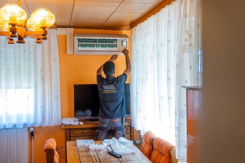 A man sets up an air conditioner in the living room next to dining room furniture, air conditioning