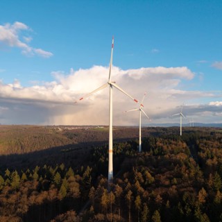 Wind turbines rise into the blue sky in a wooded area, surrounded by clouds, wind turbine, near