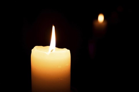 Lit candle in the dark and its reflection in the background