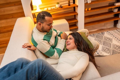 Young couple sharing a cozy evening on a sofa, smiling and talking in a warm, intimate living room,
