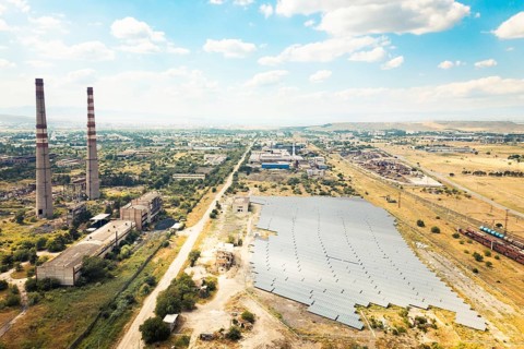 Aerial fly over view of solar power plant or farm next to abandoned industrial complex in Rustavi