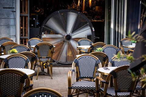A large industrial fan stands in an empty outdoor area of a café between numerous black and white