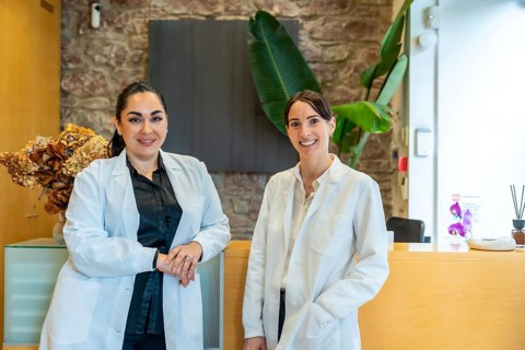 Two smiling female medical professionals wearing lab coats standing in a contemporary clinic or spa
