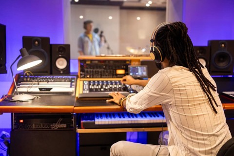 An audio engineer wearing headphones operates a mixing console in a modern recording studio,