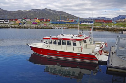 Red boat in the harbour with colourful houses in the background and mountains under a cloudy sky,