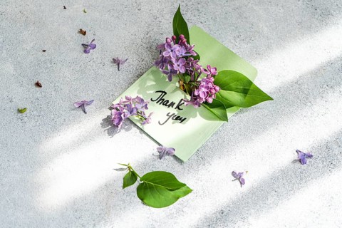 An elegant thank you card adorned with vibrant lilac flowers and green leaves lies on a textured