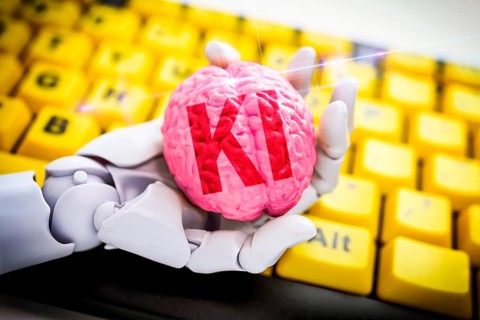 Robot hand holds a brain with the inscription AI in front of a computer keyboard, symbolic photo