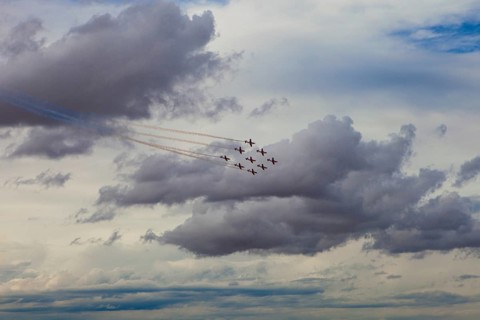 Aerobatic jets leave colorful smoke trails against a dramatic cloudy sky at an aerial show at
