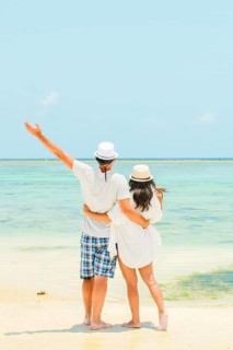 Couple stand together hugging hug enjoy arms up on white sand beach in sunny tropical destination.