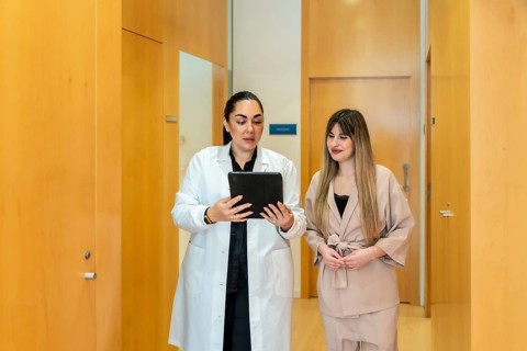 Medical professional in a white coat showing digital information on a tablet to a female patient in