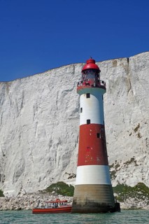 Red and white lighthouse in front of majestic white cliffs and blue sky by the sea, sight, Beachy