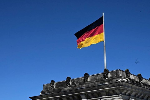 One of the towers of the Reichstag and a waving German flag against a blue sky