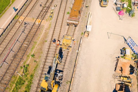 Aerial view of construction workers and machines on a railroad track in sunny weather,