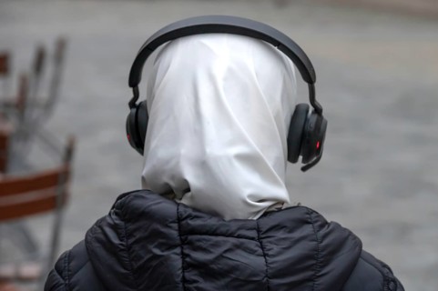 Young woman wearing headscarf and headphones in pedestrian zone, Bavaria, Germany