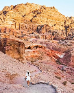 Solo traveler walking along a winding path through Petra's sandstone landscape and ancient