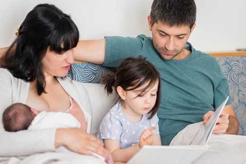 A young family is joyfully bonding at home. The mother holds a newborn baby while the father and