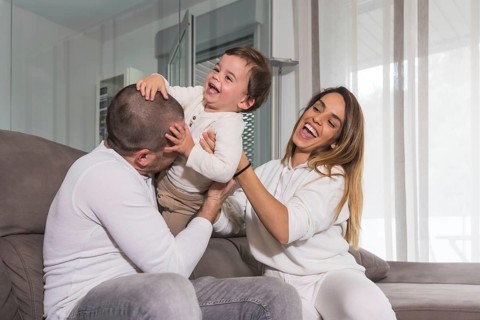 Happy family laughing and playing on the sofa with their baby